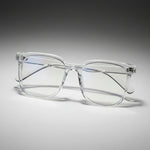 Clear eyeglasses held by a hand with a neutral background