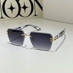 Sunglasses with gold accents on a light surface, with a cup and saucer in the background.